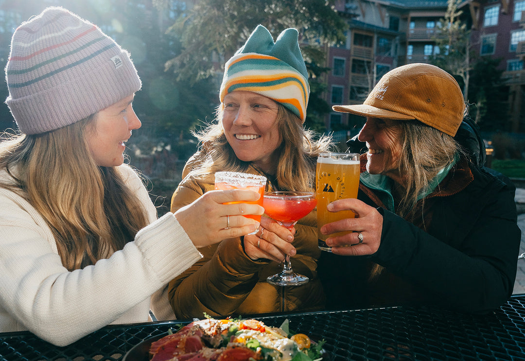 Three friends enjoying drinks together outdoors in a casual setting. Shelter Distilling Cocktails and Beer. Craft Distillery, Brewery, and Kitchen in Mammoth Lakes, CA. Dinner and drinks near Mammoth Mountain